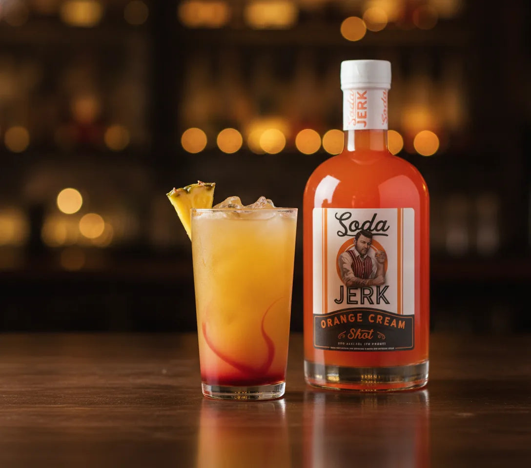 Big Stick pineapple orange creamsicle cocktail with a grenadine sunset base beside a Soda Jerk Orange Cream Shot bottle cocktail with Soda Jerk bottle